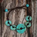 Close-up detail of a vintage ethnic style turquoise resin doughnut bracelet with brown cord. - Copper Coin Style (B23-307)