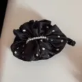 Close-up of the black polka dot satin banana hair clip, showcasing delicate pleats and pearl string detail. - Black Polka Dot
