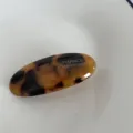 Detailed close-up of the elegant acetate tortoiseshell hair clip surface and metallic text design. - Dark Tortoiseshell