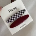 Gedetailleerde close-up van twee ovale haarspelden met een ruitjespatroon en bordeaux. - Bruinrood Gingham Lang Ovaal