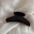 Close up of a dark minimalist hair claw clip on soft white fabric, elegant daily hair accessory. - Coffee
