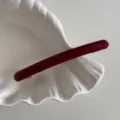 Close-up view of a slender burgundy acetate hair clip featuring a sleek metallic spring mechanism. - Red