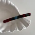 Gros plan détaillé d'une barrette à cheveux acétate marbrée sur un plat coquillage blanc. - Bleu Rouge