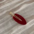 Close-up detail of the elegant red oval hair clip with gold metal accent and textured finish. - Red