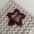 Close-up van een rode stervormige lederen haarspeld met witte stippen en een zwarte clip. - Ster / Rood Met Witte Polkadots