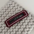 Close-up detail van de stijlvolle leren haarklem met witte rand op gebreide stoftextuur. - Rechthoek / Rood met wit web