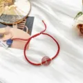 Gros plan détail du bracelet tressé en cordon rouge fait main avec un pendentif en cristal rose. - Boucle Ping'an Quartz Fraise