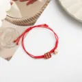 Red braided rope bracelet detail featuring a square pendant and golden bell design. - Peace and Joy