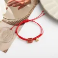 Rotes geflochtenes Armband mit quadratischem Glücksanhänger und Glocke für das Neujahrsfest. - Grenzenloses Glück