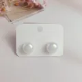 Close-up shot of elegant iridescent mermaid pearl stud earrings on clean white card display. - M / White