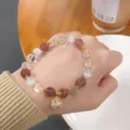 Close up detail of beaded bracelet with strawberry quartz cat eye beads and ladybug charm. - Strawberry Quartz