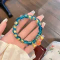 Vista dettagliata del bracciale di perle di vetro blu con foglia d'oro e graziosi ciondoli dorati. - Smalto Foglia d'Oro Blu