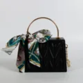 Stylish black top handle crossbody bag with gold round metal handle and silk scarf accessory. - Black
