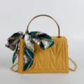 Yellow structured handbag with metal top handle, chain strap and elegant green silk scarf decor. - Yellow