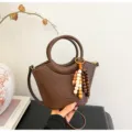 Stylish brown leather bucket handbag with top handle and wooden bead charm for women. - Brown with Pendant