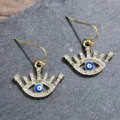 Close-up detail of rhinestone evil eye hook earrings with blue enamel accent on slate. - Eyelash Round Eye Style (A24-262)