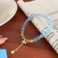 Detailed view of refreshing blue natural stone beaded bracelet with cute gold pendant detail. - Aquamarine with Beeswax and Fishtail
