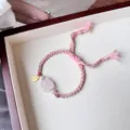 Close-up detail of the pink braided charm bracelet featuring a crystal pixiu and pearl accent. - Rose Quartz Nine-Tailed Fox