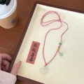 Delicate natural white agate ruyi necklace detail, featuring pink cord and green bead charms. - Peach Pink