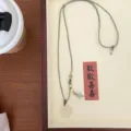 Detail view of a Chinese-style white agate necklace featuring green braided cord and gold beads. - Bean Green