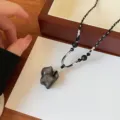 Detailed close-up shot of Chinese style natural obsidian pendant with woven clavicle chain. - Cat