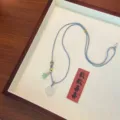 Detail view of white agate ruyi necklace pendant with blue cord and multi-gem accents. - Silver Gray