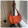 Detail view of the stylish orange crescent shoulder bag featuring chic metallic buckle hardware. - Orange Red