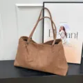 Brown suede tote bag detail view, stylish commuting shoulder bag on dark wooden table. - Brown