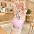 Pink apple keychain detail with faux pearl bracelet and heart-shaped metal clasp, close-up view. - Pink Apple