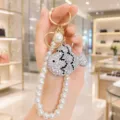 Rhinestone crystal fish keychain detail with elegant pearl strap and golden hardware shine. - White