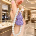 Detail view of luxury pearl phone strap with sparkly purple crystal gourd pendant and metal keychain. - Purple
