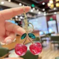 Close-up of sparkling glitter cherry bag charm with crystal leaves and gold keychain. - Red Glitter Green Leaf Cherry