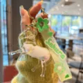 Detailaufnahme des süßen flüssigen Treibsand-Pferd-Schlüsselanhängers mit grünem Sakura-Gurt. - Weiß
