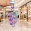 Close-up detail of a purple acrylic grape cluster keychain pendant held by hand in a bright mall. - Purple Grape With Green Leaves