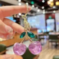 Close-up of sparkling glitter purple cherry keychain with green crystal leaves and gold hardware. - Purple Glitter Green Leaf Cherry