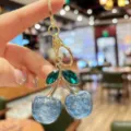 Stylish glitter blue cherry bag charm keychain with gold hardware and green crystal leaves. - Blue Glitter Green Leaf Cherry