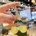 Close-up detail of sparkling yellow cherry keychain with green crystal leaves and gold metal ring. - Yellow Glitter Green Leaf Cherry