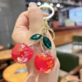 Detail shot of a stylish red cherry keychain, crystal leaves, gold metal bag pendant charm. - Red Iridescent Green Leaf Cherry