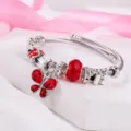 Vista dettagliata del raffinato bracciale con ciondoli in acciaio e farfalle di cristallo rosso. - Rosso