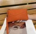 Dettaglio pochette in pelle arancione con trama fine, design a Busta e cinturino. - Arancione