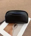 Details of the black leather clutch bag featuring silver zipper and white stitching accents. - Black