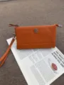 Oranger Leder-Münzbeutel mit Handschlaufe und Kleeblatt-Metalldekor für den Alltag. - Orange