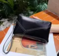 Detailed view of black genuine leather clutch bag with wrist strap and stylish stitching. - Black