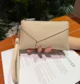 Detail view of a beige leather wristlet pouch with zipper and strap, elegant and compact design. - Off White