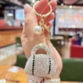 Detailed view of sparkly rhinestone handbag keychain with pearl pendant and gold ring. - White