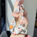 Detailed close-up shot of colorful pastel beaded phone charm with camera and letter design. - Orange