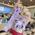 Detailed view of a purple flower liquid floating keychain with Sakura strap and gold hardware. - Purple