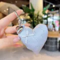 Detailed closeup of cute heart-shaped fabric bag pendant with bow and rhinestones. - Gray