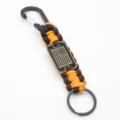 Vista detallada del llavero de paracord hecho a mano con etiqueta de metal de bandera. - Naranja y Negro