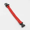 Red paracord survival bracelet with black plastic buckle, outdoor emergency gear detail. - Red